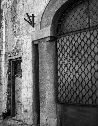 black and white photograph of a building facade featuring old, textured brickwork and a doorway secured with a metal mesh screen in Bucharest Romania
