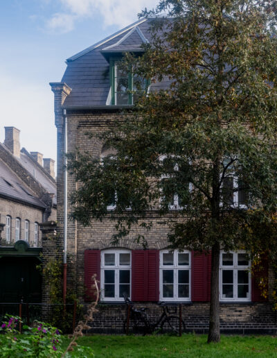 historic townhouse situated in Copenhagen, Denmark. The property features traditional architectural elements such as light-colored brickwork and red wooden shutters on the windows.