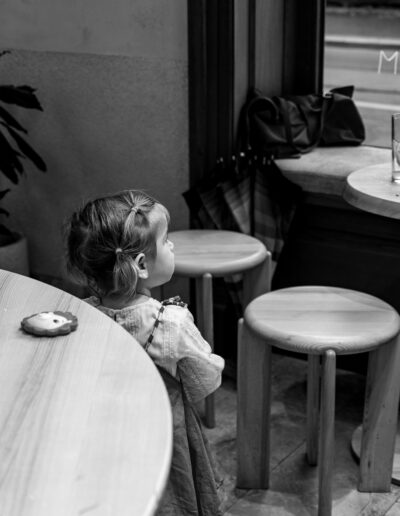 black-and-white portrait of a young girl sitting at a cafe table