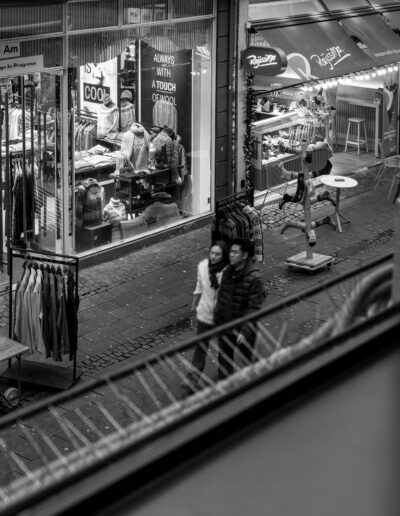 two people walking together on a cobblestone street at night, viewed from an elevated perspective