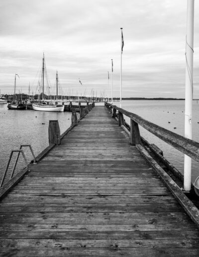 photograph of a wooden pier or jetty extending into a calm harbor with sailboats docked nearby in Roskilde Denmark