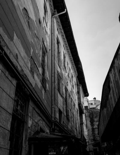 Black and white photograph depicting a narrow alleyway or courtyard surrounded by weathered, older buildings in Bucharest Romania